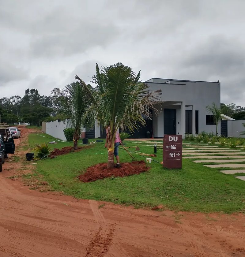 Paisagismo para casas de campo em Arandu: casa moderna com palmeiras e caminho de pedras no gramado, por Greg Garden Paisagismo